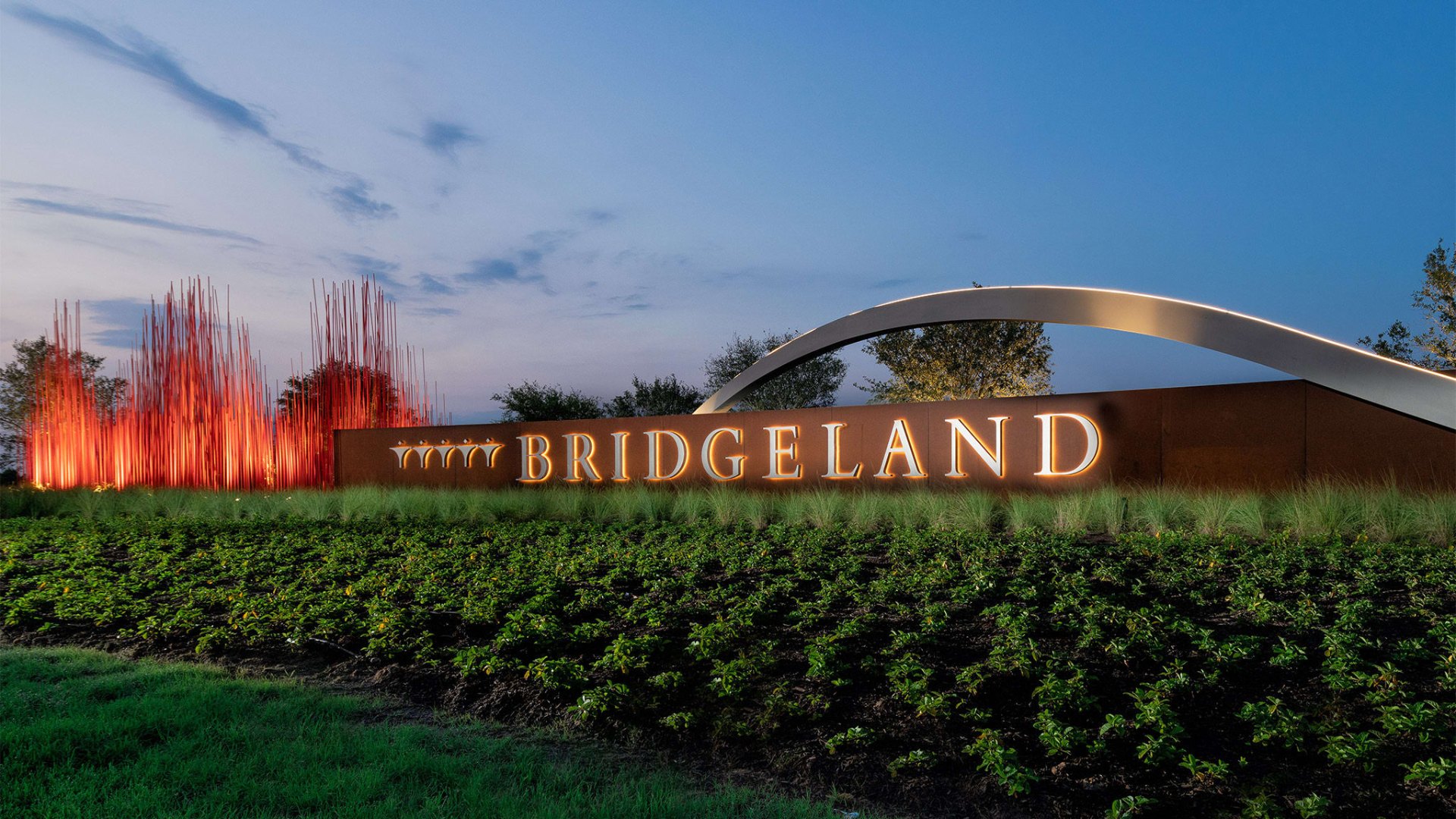 Bridgeland community entrance sign at dusk with illuminated signage and red sculptural rods
